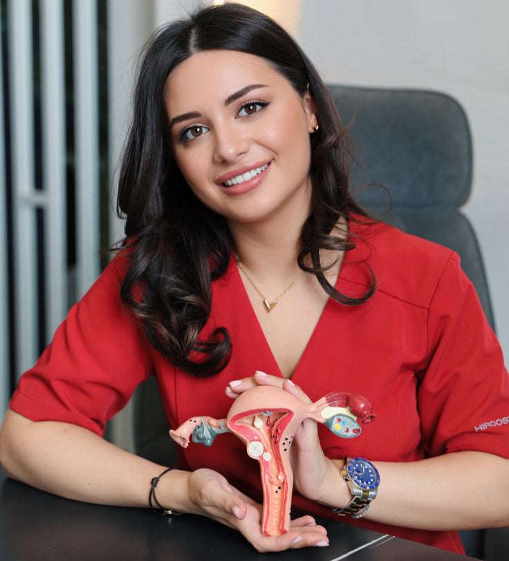 Woman in a red shirt holding a model of the female reproductive system.